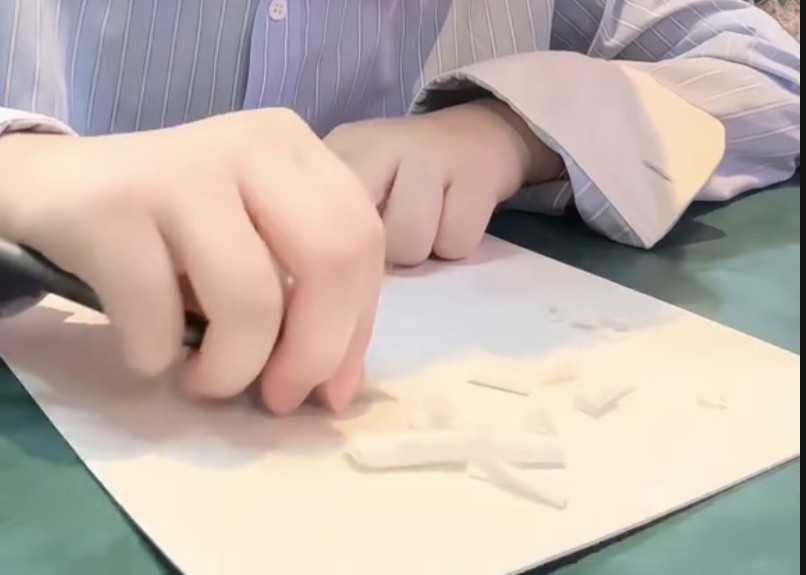 Hands carving a portrait from a sheet of paper